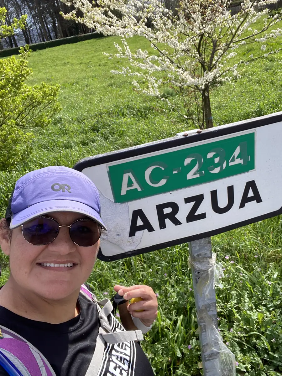 Estela smiling beside the Arzúa town sign